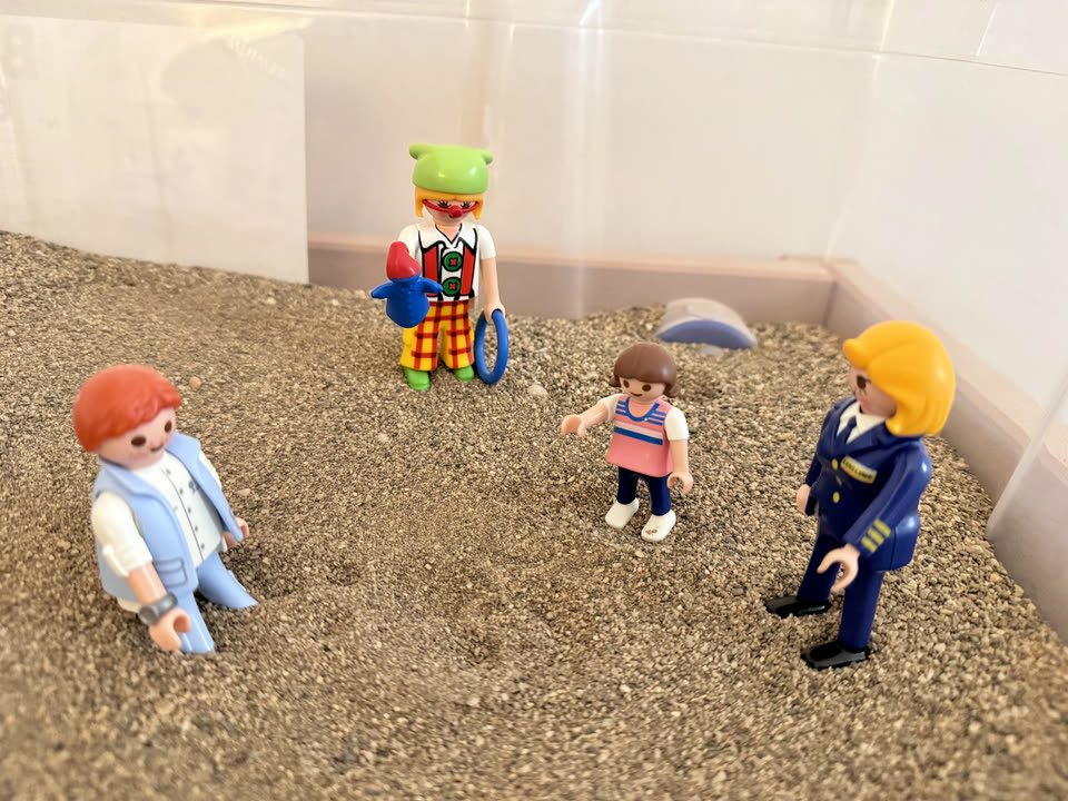 Caja de arena de terapia con cuatro figuras colocadas sobre la arena.