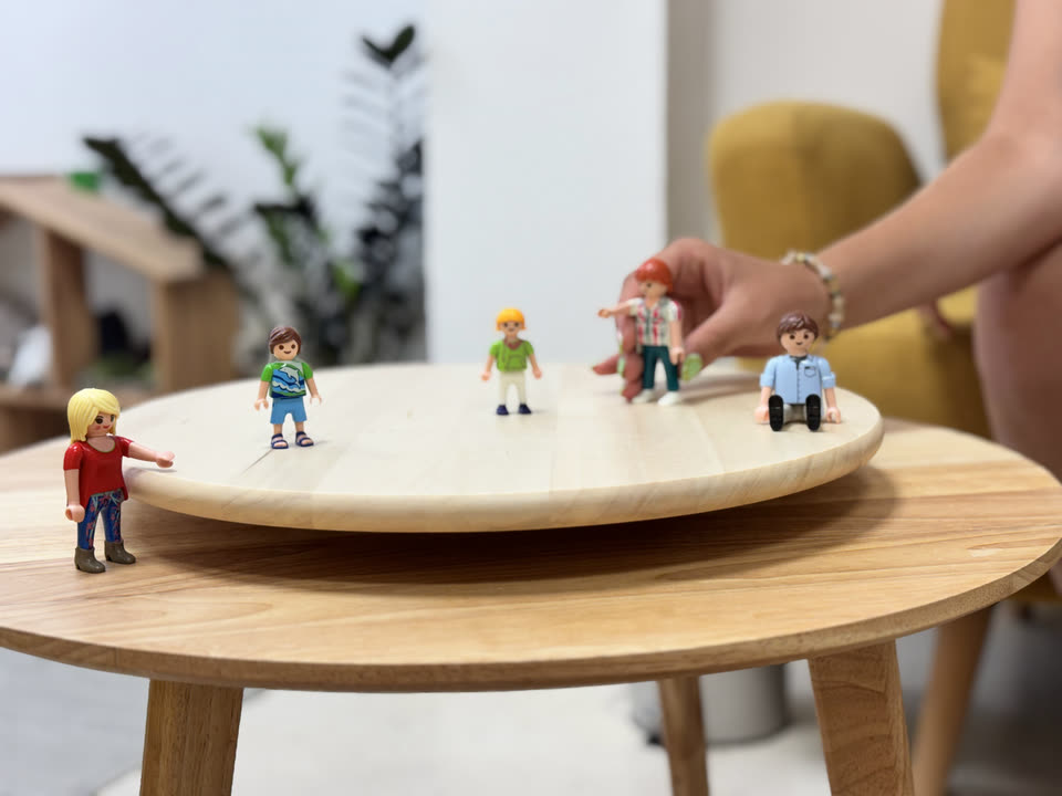Figuras Playmobil colocadas sobre una bandeja giratoria de madera durante un trabajo proyectivo familiar.